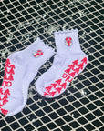 Pair of white lobster-crest grip socks for barre class laid on a net over water with red lobster grip soles.