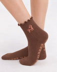 Model wearing The Doodle Grip Sock, crossed feet showing the paw-print grip soles and embroidered golden doodle on the ruffle cuff