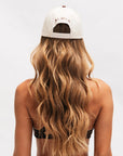 Back view of a woman with blonde hair wearing a cream ALMLA cap from the reformer pilates grip socks brand.
