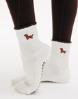 Back view of feet in brown leggings wearing white dachshund non slip yoga socks with brown ruffle cuffs and grips.