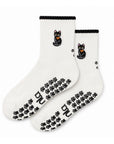 The Black Cat Grip Sock pair, cream crew grip socks with an embroidered black cat wearing an orange bow, black scalloped cuff and black paw print grips