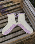 Cream and lavender bow grip socks laid on weathered wood in a blooming lavender field