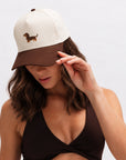 Woman adjusting the brim of The Doxie Brown Hat, a cream and brown embroidered dachshund cap