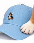 Corgi paw resting on the brim of The Tri-Color Corgi Denim Hat, close up of the embroidered tri-color corgi