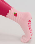 Close-up of a pointed foot wearing a pink strawberry anti slip pilates sock with grip dots on the sole.