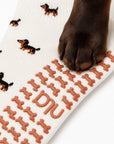 A real dog's paw resting on the dachshund-shaped grip sole of The Dachshund Grip Sock, showing the all-over dachshund print