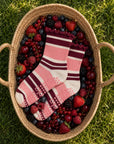 Raspberry cream striped grip socks styled in a basket of fresh summer berries