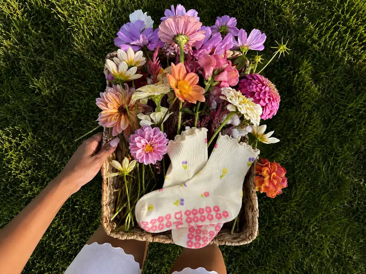 Cream floral patterned grip socks with pink flower grips in a basket of dahlias on grass