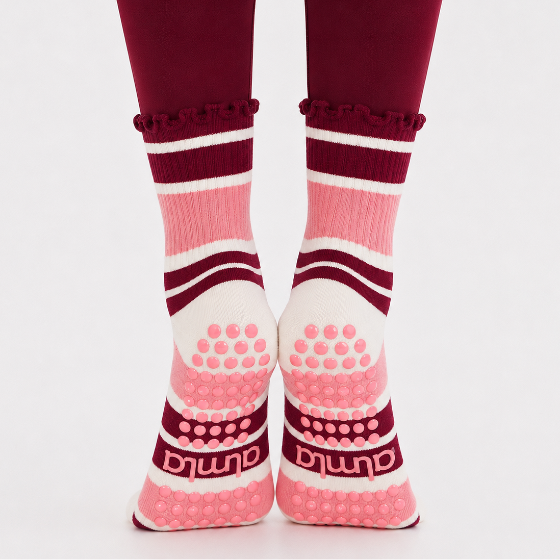 Pink and burgundy grip socks worn on feet positioned on toes showing the sole and grip pattern on burgundy leggings