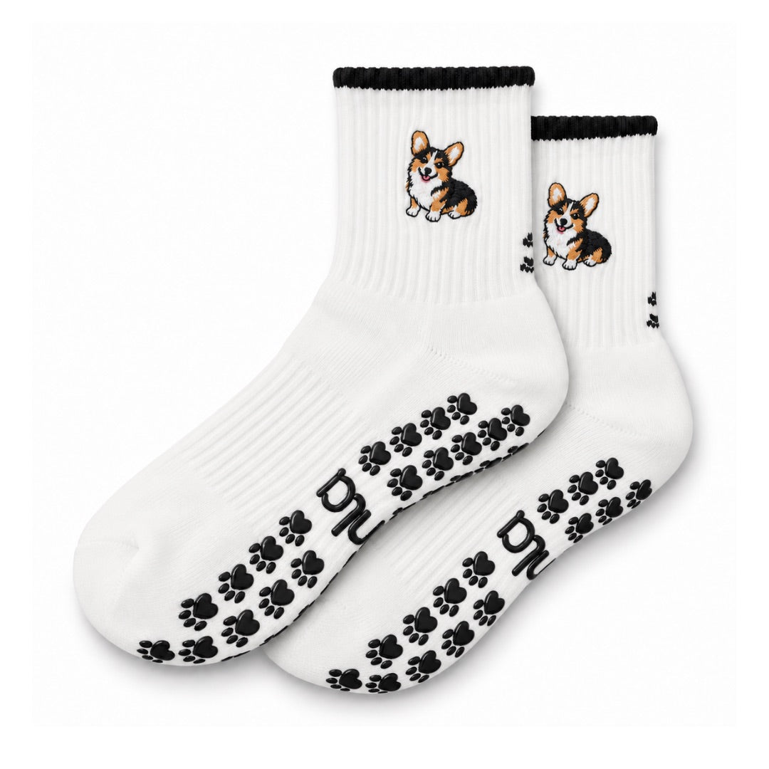 The Tri Color Corgi Grip Sock in white with a black cuff, embroidered tri-color corgi, and paw-shaped non-slip grips, laid flat on a white background