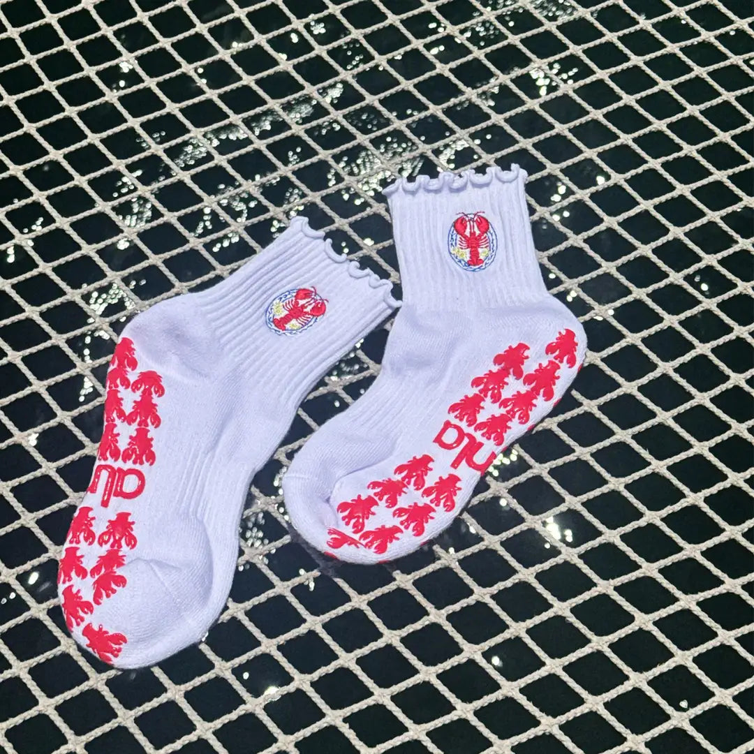 Pair of white lobster-crest grip socks for barre class laid on a net over water with red lobster grip soles.