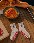 Pair of white lobster-crest sticky socks for barre class on a boat deck beside lobster pasta and a book.