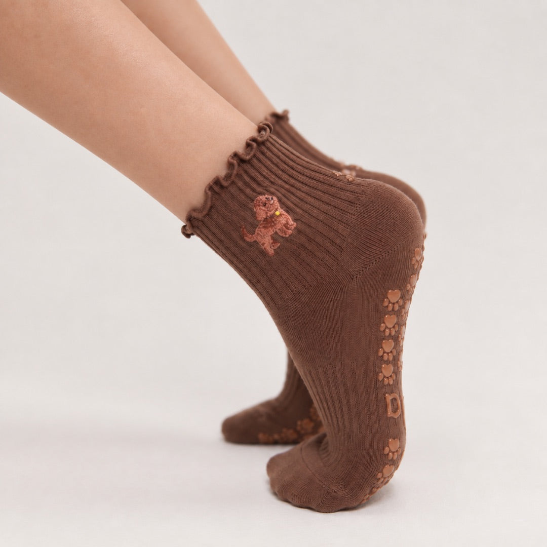Model wearing The Doodle Grip Sock on pointed toes, side profile showing the paw-print grip soles and embroidered golden doodle