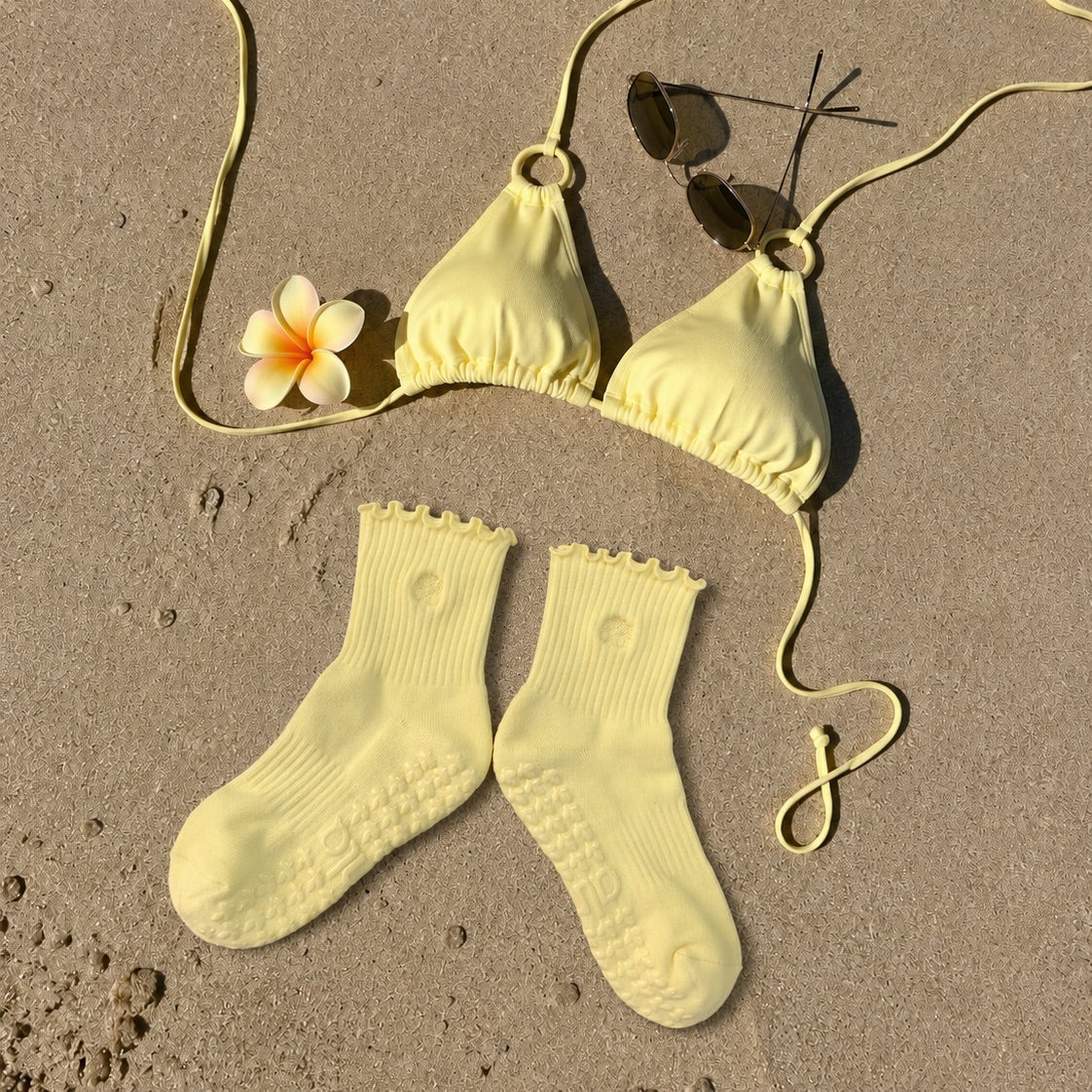 Butter yellow grip socks on the sand with a matching bikini and sunglasses