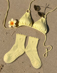 Butter yellow grip socks on the sand with a matching bikini and sunglasses