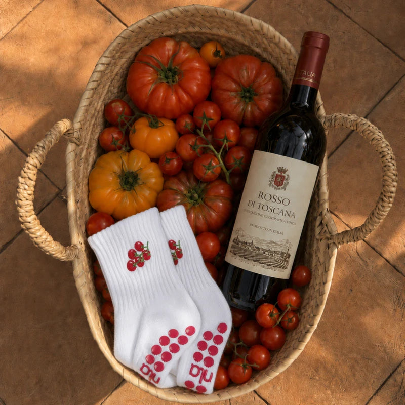 Pair of white cherry-tomato cute pilates grip socks in a basket with heirloom tomatoes and a bottle of red wine.