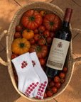 Pair of white cherry-tomato cute pilates grip socks in a basket with heirloom tomatoes and a bottle of red wine.