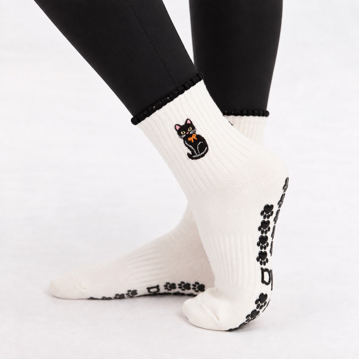 Side view of the Black Cat Grip Sock on foot showing the embroidered black cat, scalloped cuff and paw print grips