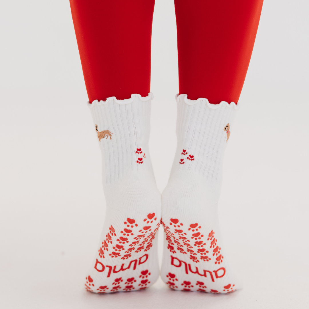 Back view of Doxie Grip Socks on feet showing red heart paw prints on the ankle, red paw print grips and almla logo
