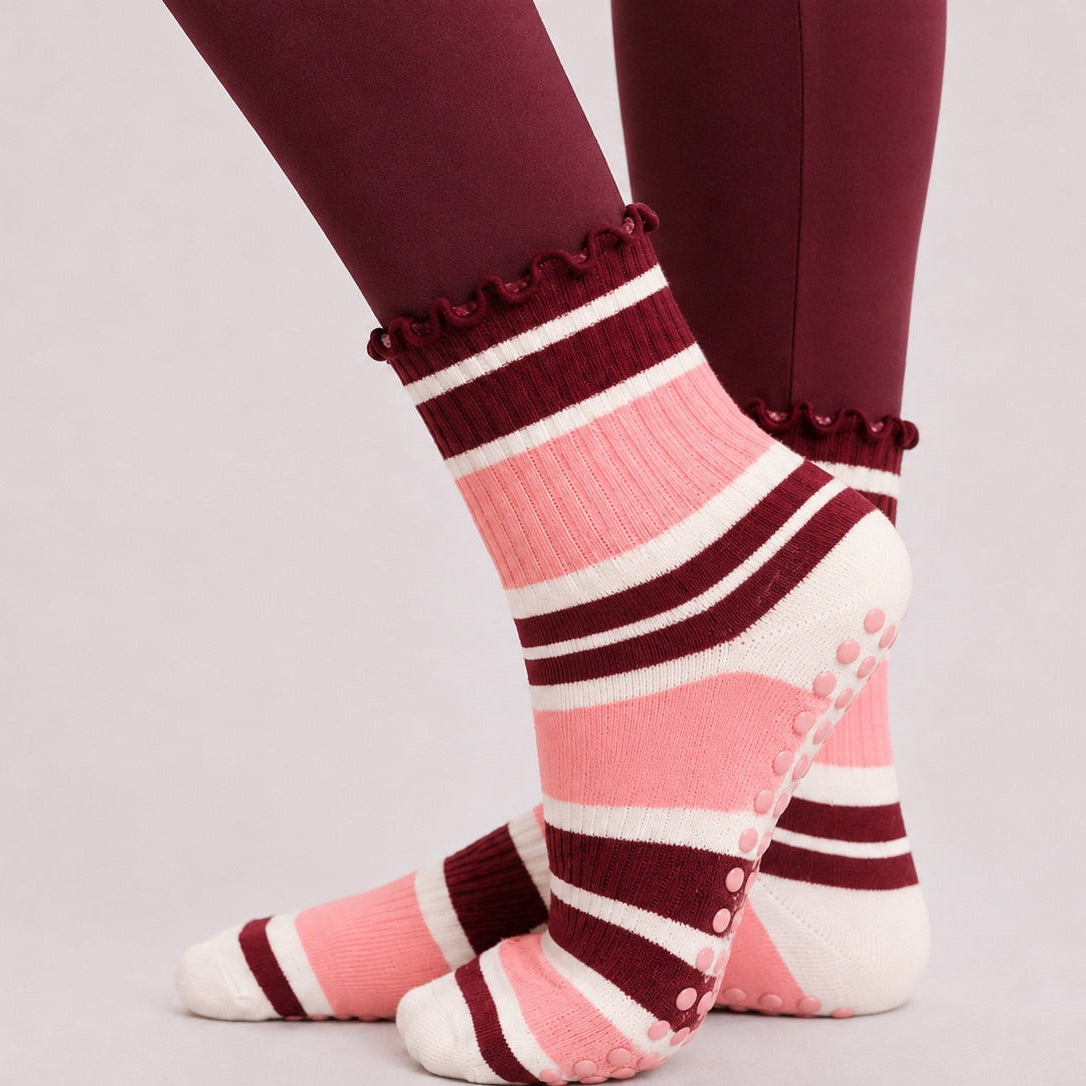 Pink and burgundy striped pilates grip socks worn with burgundy leggings, side view