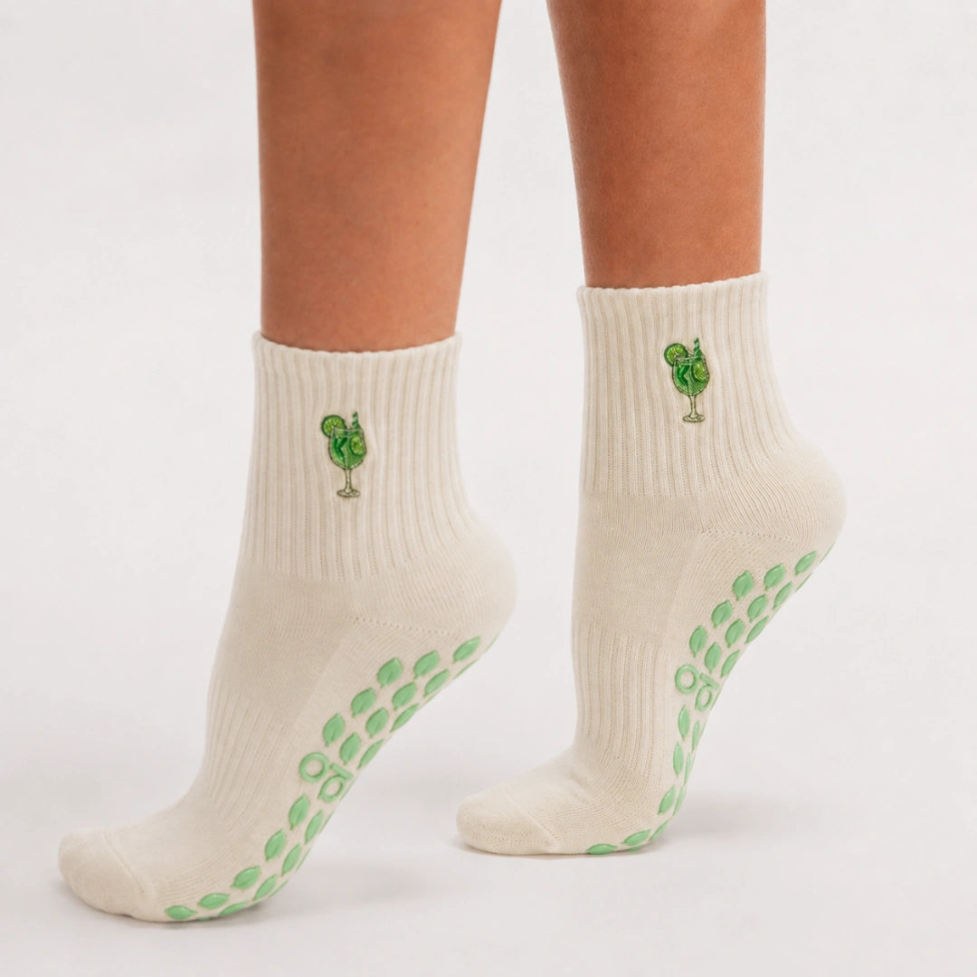 Side view of feet on tiptoe wearing cream cocktail-embroidered sticky socks barre with green grip soles.
