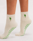 Side view of feet on tiptoe wearing cream cocktail-embroidered sticky socks barre with green grip soles.