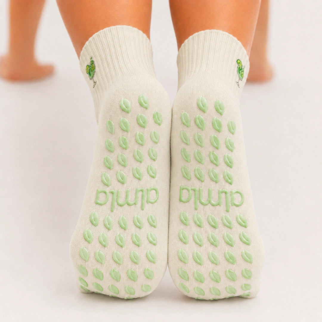 Back view of raised feet wearing cream cocktail-embroidered grippy socks for barre with pale green grip dots.