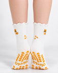 Model standing in a pair of The Orange Cat Grip Sock, front view showing the embroidered orange tabby cat on each ankle and paw-print grip soles with the Almla logo