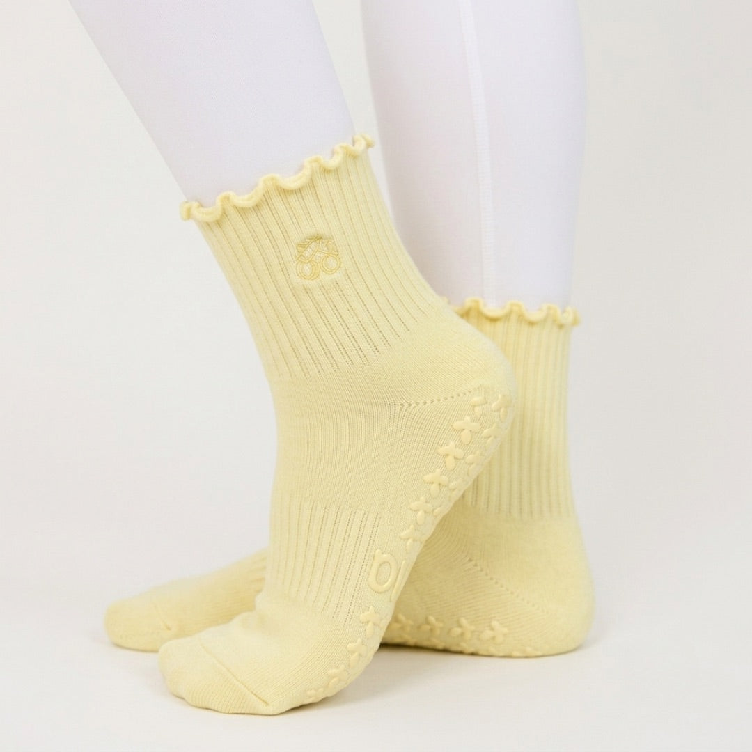 Butter yellow ribbed pilates grip socks worn with white leggings, side view of ruffle cuff