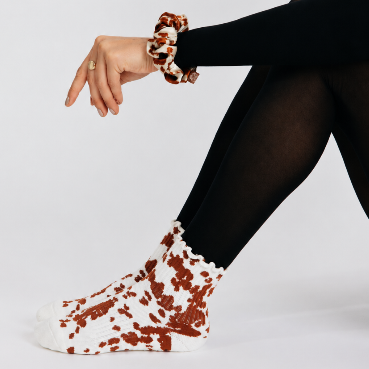 Cowhide grip sock and silk scrunchie set laid out together, coordinated animal print for Pilates, barre, and everyday
