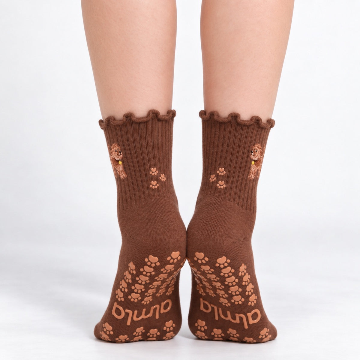 Model standing in a pair of The Doodle Grip Sock, front view showing the embroidered golden doodle on each ankle and paw-print grip soles with the Almla logo