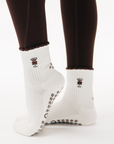 Back view of feet in brown leggings wearing white espresso-martini sticky socks yoga with brown ruffle cuffs.