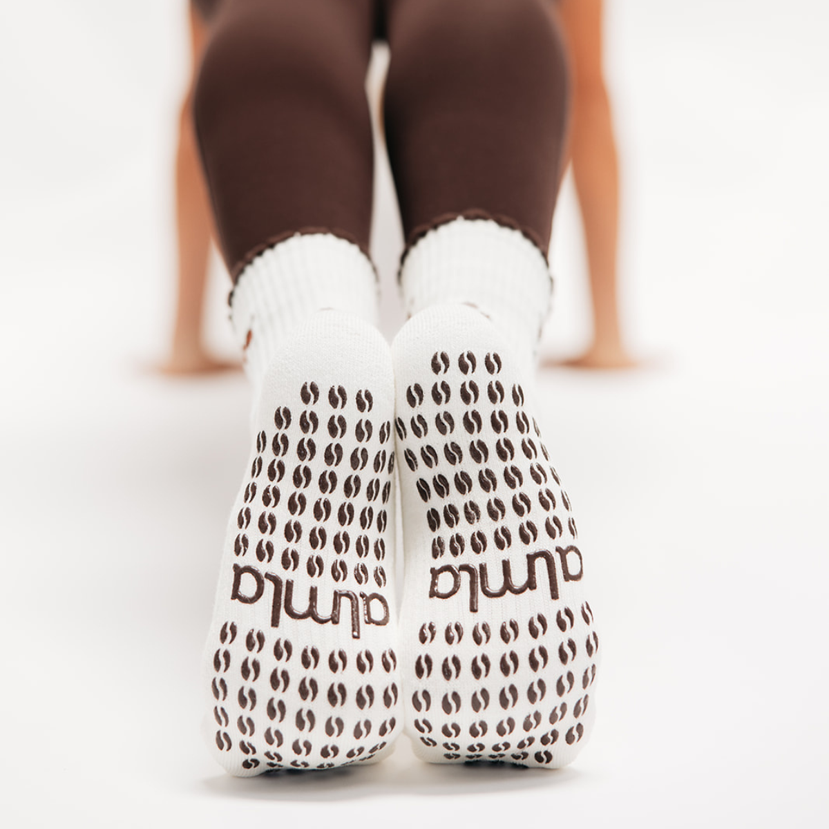 Back view of raised feet in brown leggings wearing white non skid socks for pilates with brown coffee-bean grips.