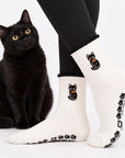 Black cat sitting next to a model wearing the Black Cat Grip Sock with embroidered cat and orange bow