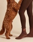 A golden doodle standing on hind legs beside a model wearing leggings and The Doodle Grip Sock, showing the embroidered doodle design and paw-print grip soles