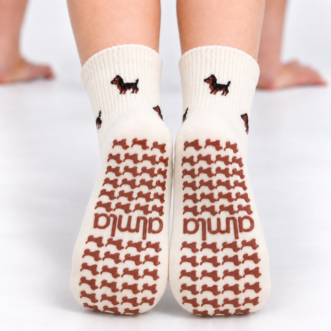 Back view of The Dachshund Grip Sock worn on both feet, showing the all-over dachshund print and dachshund-shaped grip soles with the Almla logo