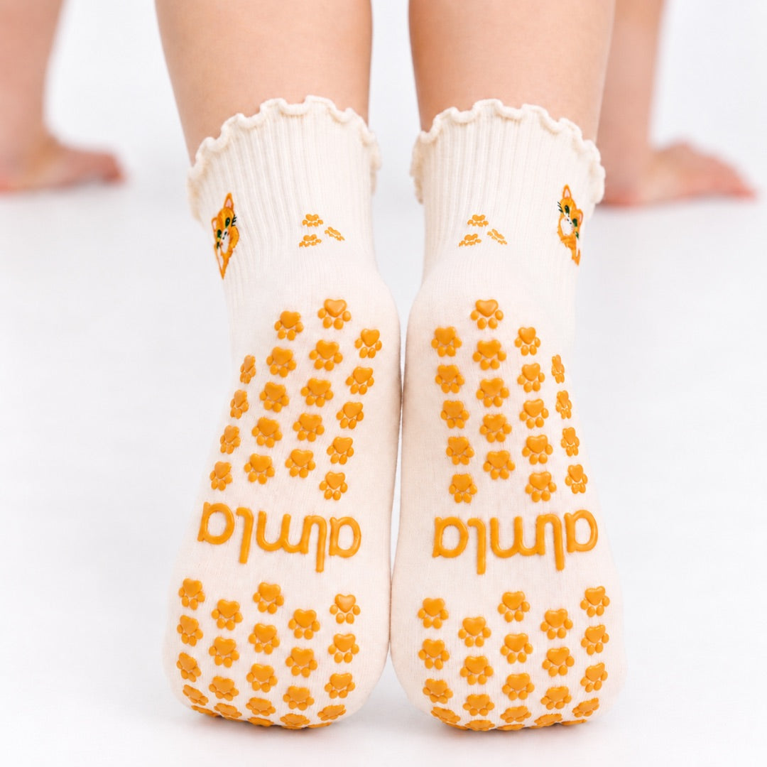 Back view of The Orange Cat Grip Sock worn on both feet, showing the full paw-print grip pattern and Almla logo on the soles