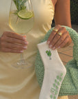 Woman in a yellow dress holding a green knit bag and a white margarita-embroidered yoga sock with grips.