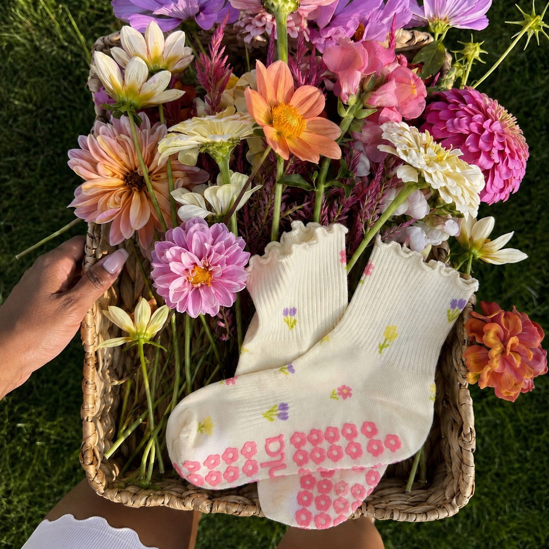 Cream floral grip socks tucked into a basket of fresh dahlias on green grass