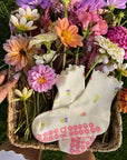 Cream floral grip socks tucked into a basket of fresh dahlias on green grass