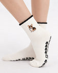Model wearing The Tri Color Corgi Grip Sock, crossed feet showing the paw-print grip soles and embroidered tri-color corgi on the cuff