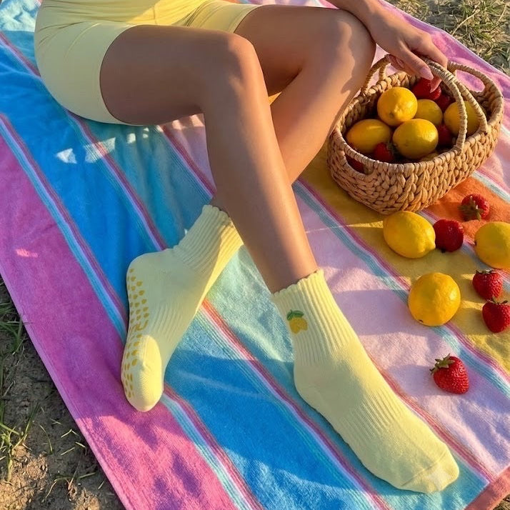Woman's legs resting on a striped beach towel wearing yellow lemon-print non slip pilates socks.