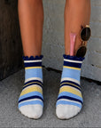 Blueberry lemon striped grip socks worn outdoors with sunglasses against a brick wall