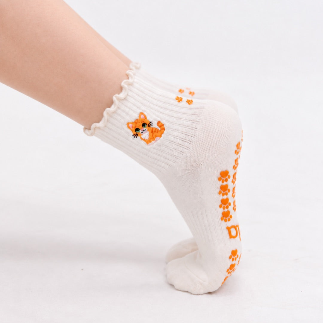 Model wearing The Orange Cat Grip Sock on pointed toes, side profile showing the paw-print grip soles and embroidered orange tabby cat