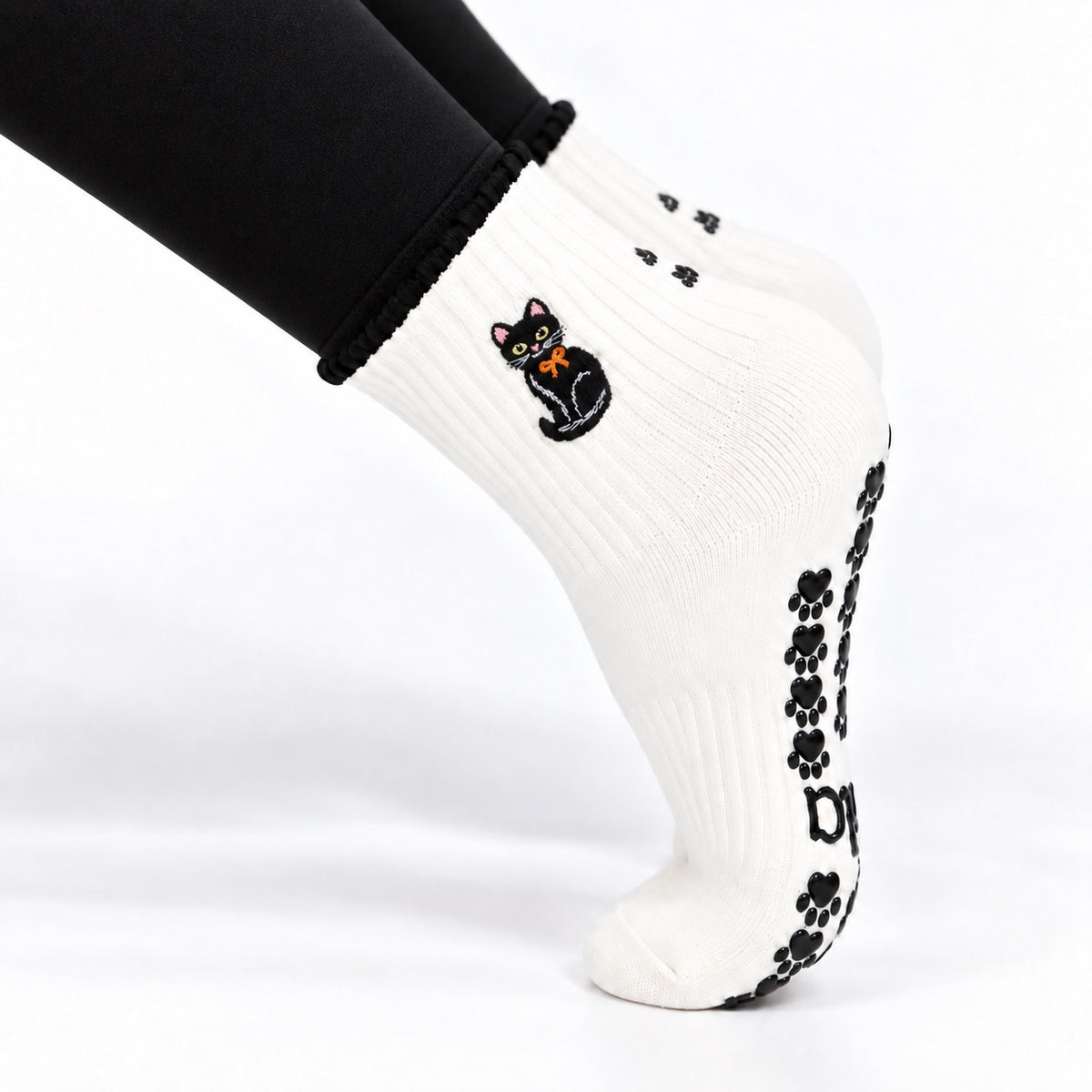 Black Cat Grip Sock worn on a pointed foot showing the embroidered black cat and paw prints on the back of the ankle