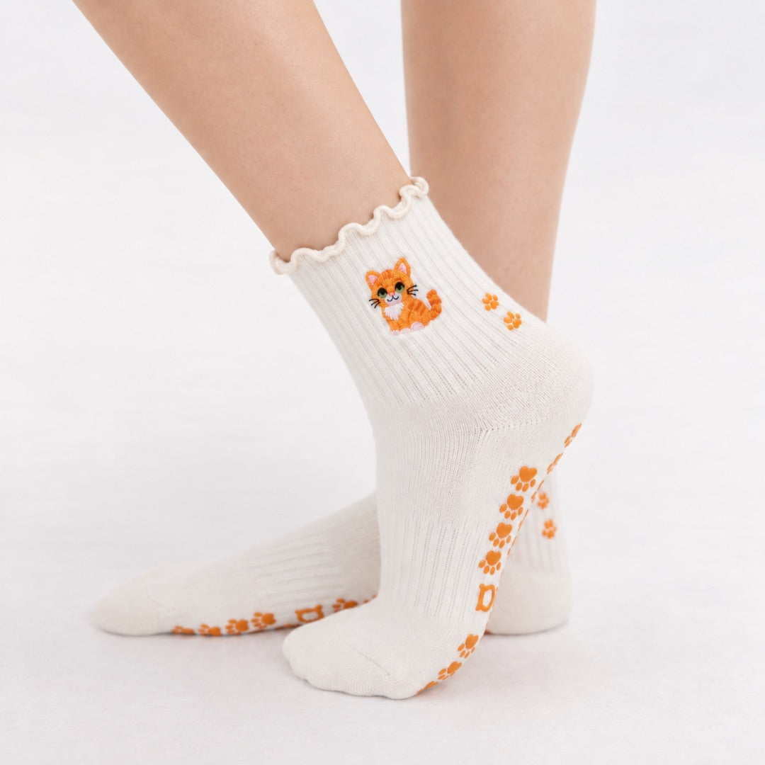 Model wearing The Orange Cat Grip Sock, crossed feet showing the paw-print grip soles and embroidered orange tabby cat on the ruffle cuff