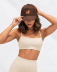 Woman in cream activewear adjusting The Goldendoodle Brown Hat with embroidered goldendoodle