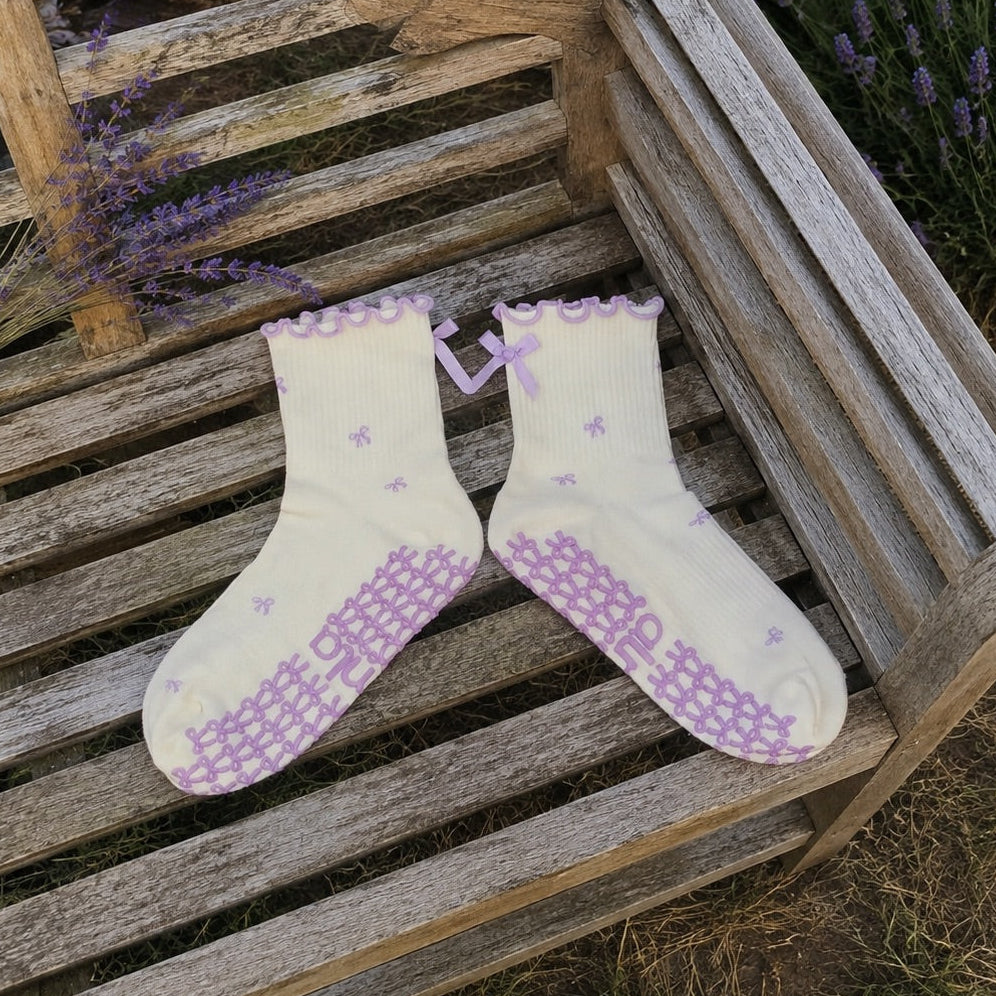 Cream and lavender bow grip socks laid on weathered wood in a blooming lavender field
