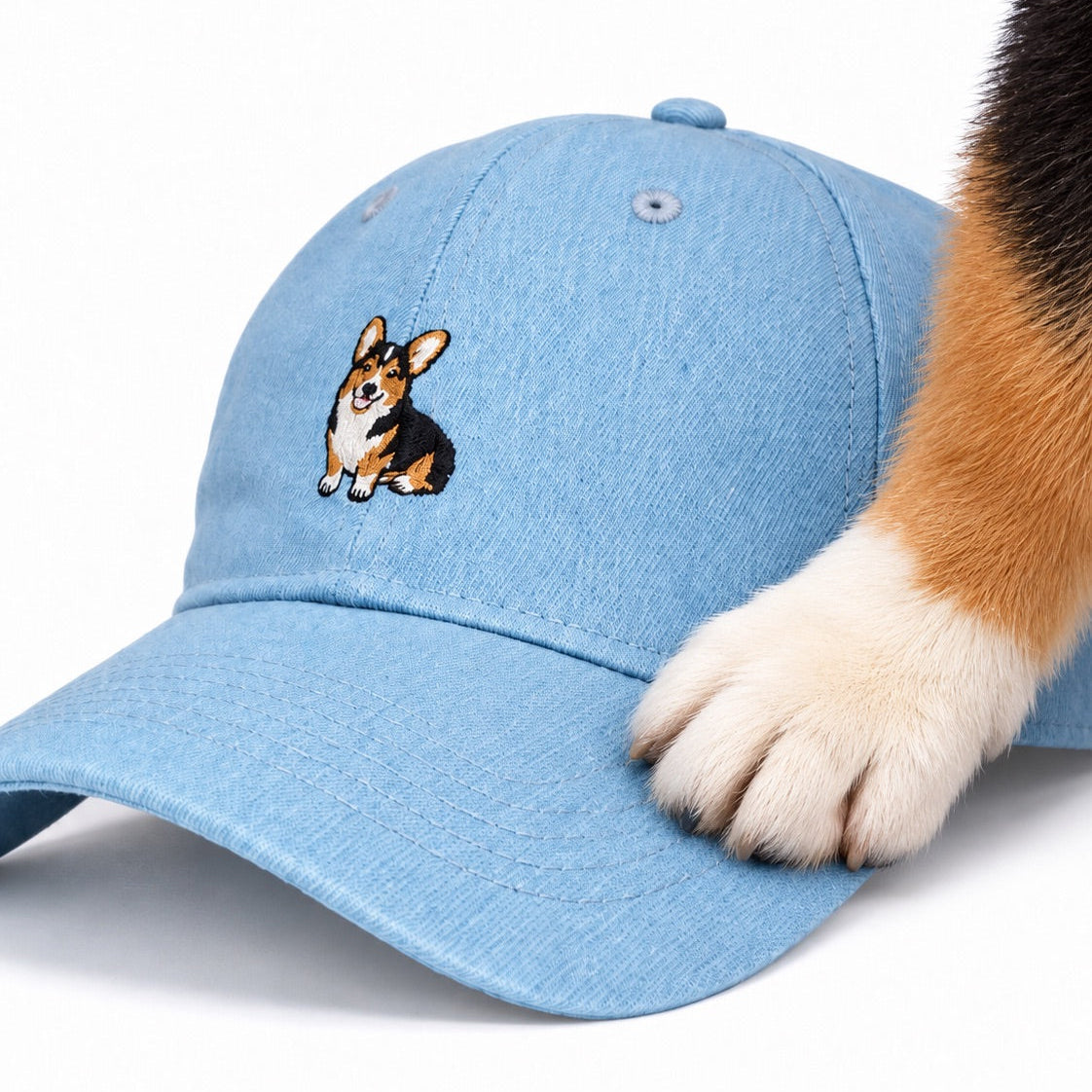 Corgi paw resting on the brim of The Tri-Color Corgi Denim Hat, close up of the embroidered tri-color corgi