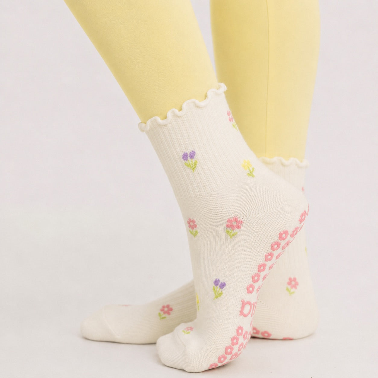 Cream floral pilates grip socks worn with butter yellow leggings, side view of ruffle cuff
